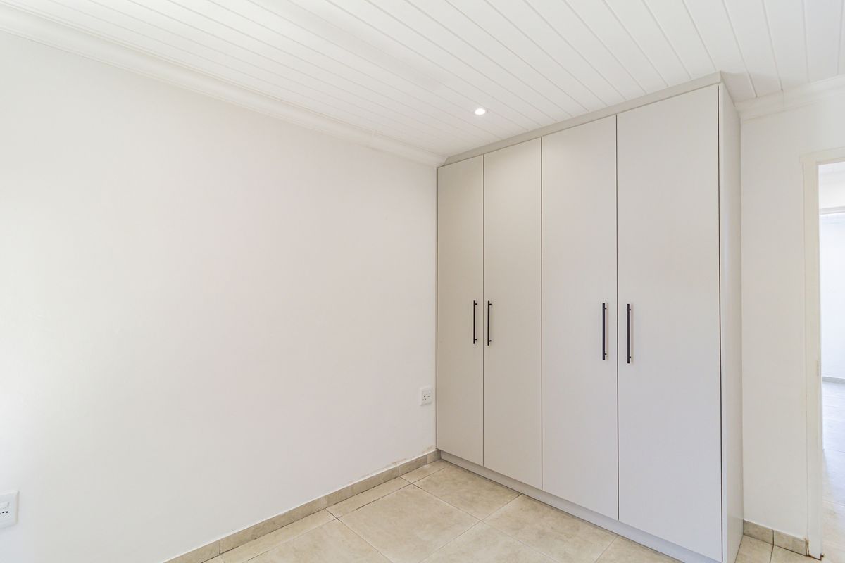 A clean, bright bedroom featuring built-in floor-to-ceiling cabinetry, tiled flooring, and a classic tongue-and-groove ceiling finish.
