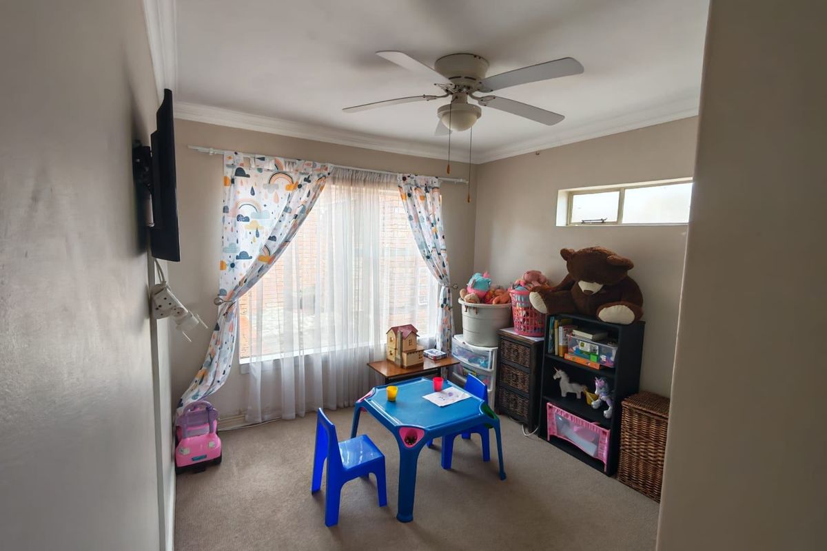 A functional bedroom featuring neutral carpeting, a ceiling fan, and a high-set window, currently utilized as a children's play area.