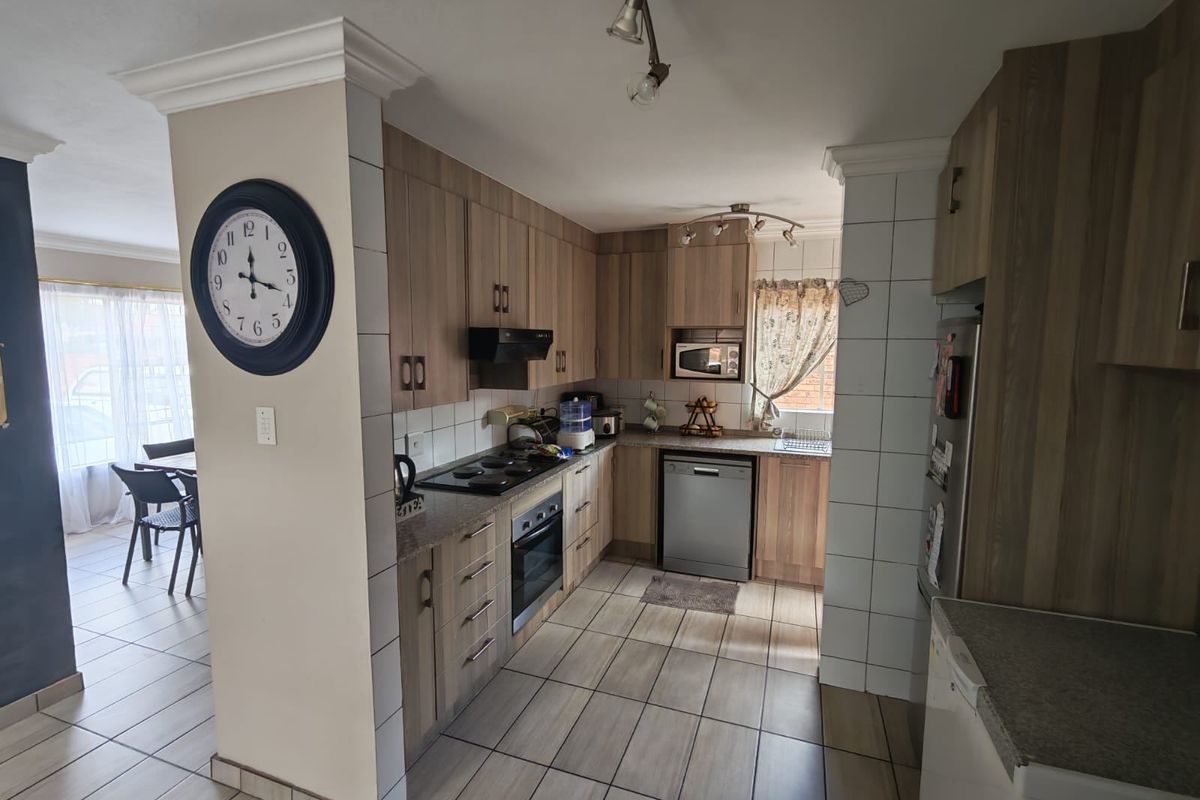 Functional kitchen featuring wood-look cabinetry, tiled splashbacks, built-in oven, hob, and extractor fan, with tiled flooring throughout.