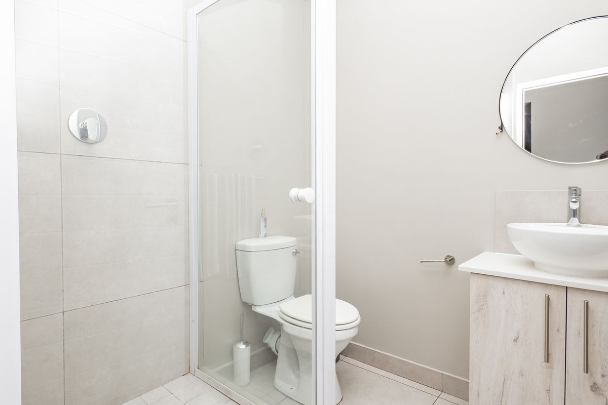 Modern bathroom featuring a glass-enclosed shower, a white ceramic toilet, and a vanity unit with a vessel sink and round mirror.