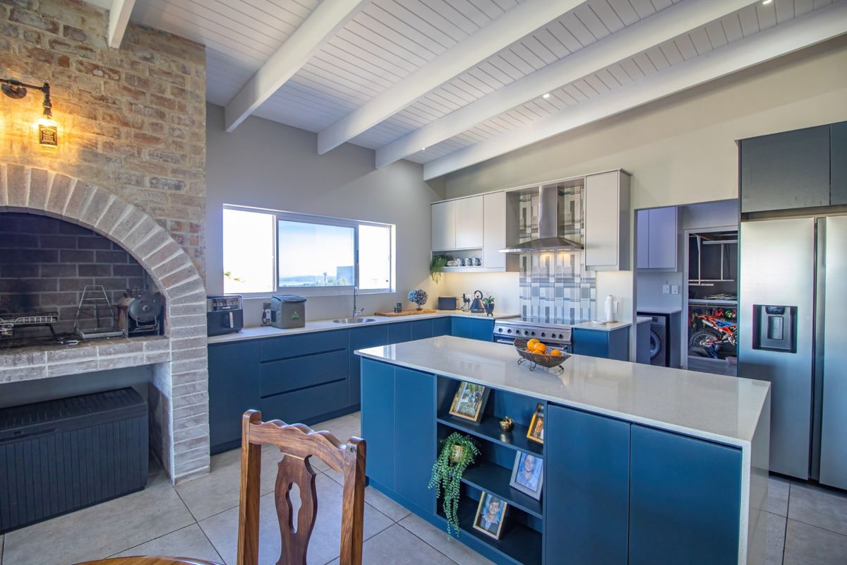 Modern kitchen featuring a central island, stone countertops, built-in cabinetry, stainless steel extractor fan, and an integrated brick fireplace feature.