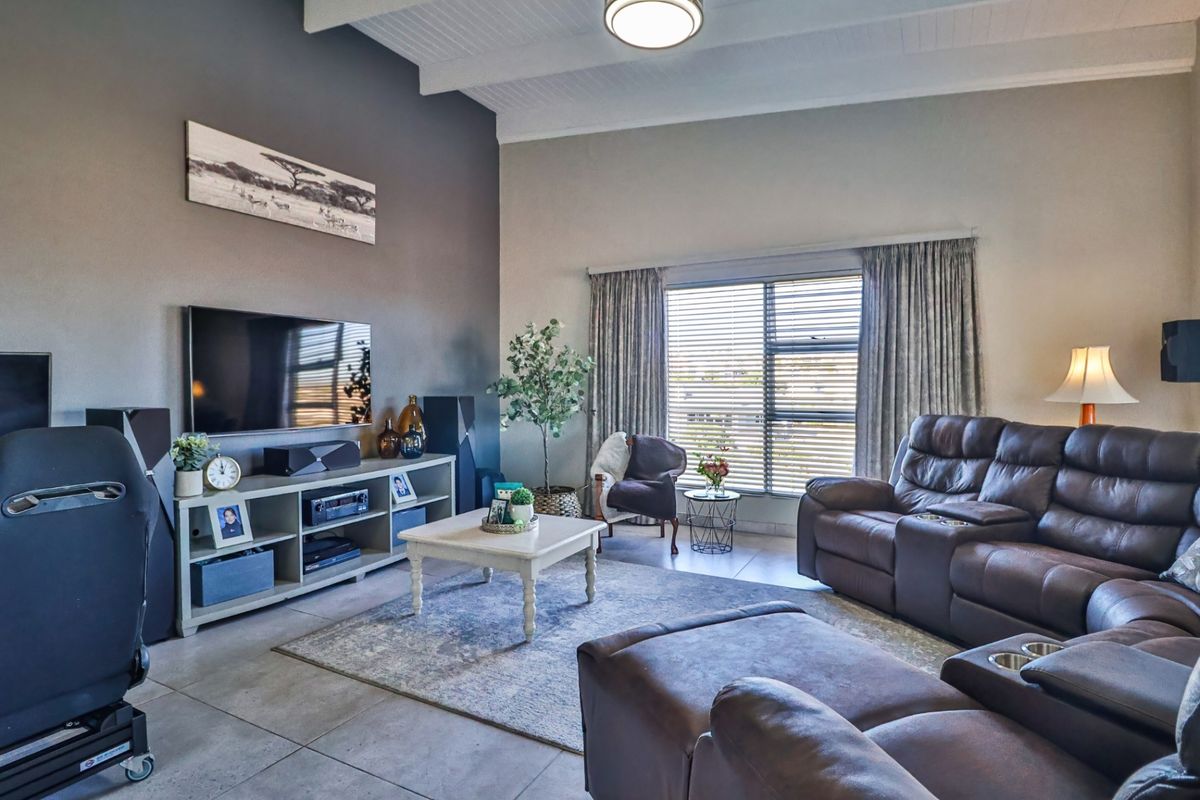 Spacious living room featuring high vaulted ceilings, large windows with blinds, and neutral tiled flooring, creating a comfortable and well-lit family space.