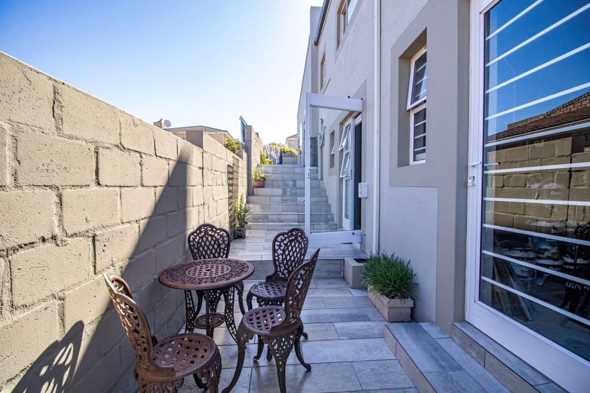 A paved rear courtyard area featuring a boundary wall, tiled flooring, and steps leading to an elevated section of the property.