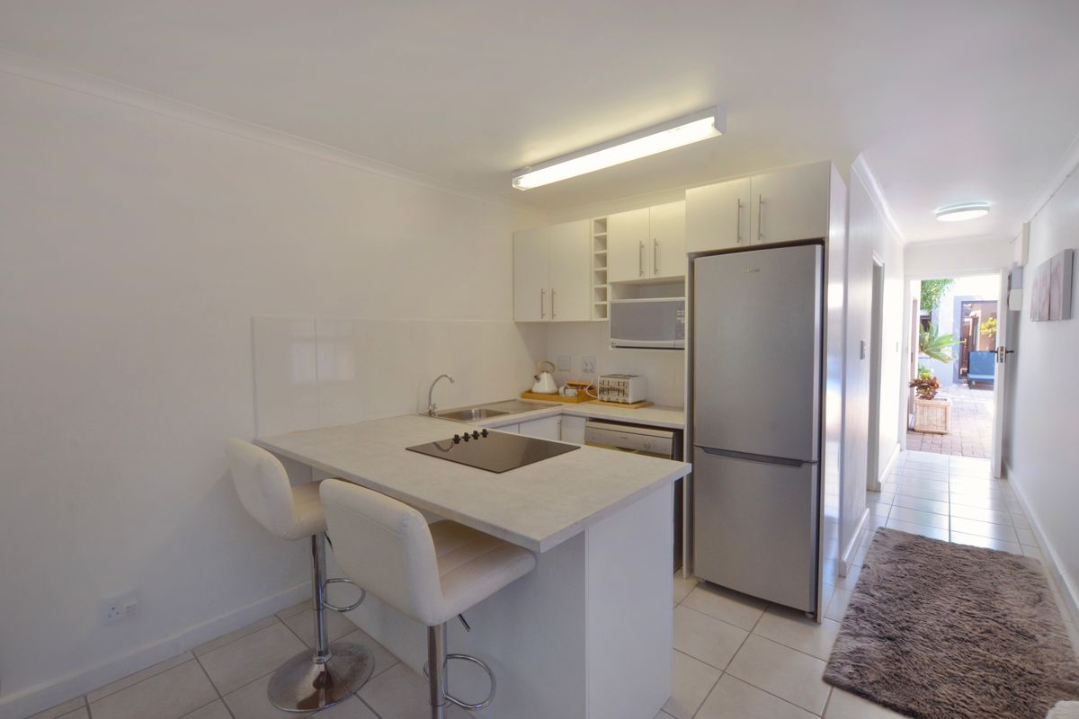 Compact kitchen featuring white cabinetry, a breakfast bar with integrated cooktop, stainless steel sink, and tiled flooring, leading to an outdoor patio area.