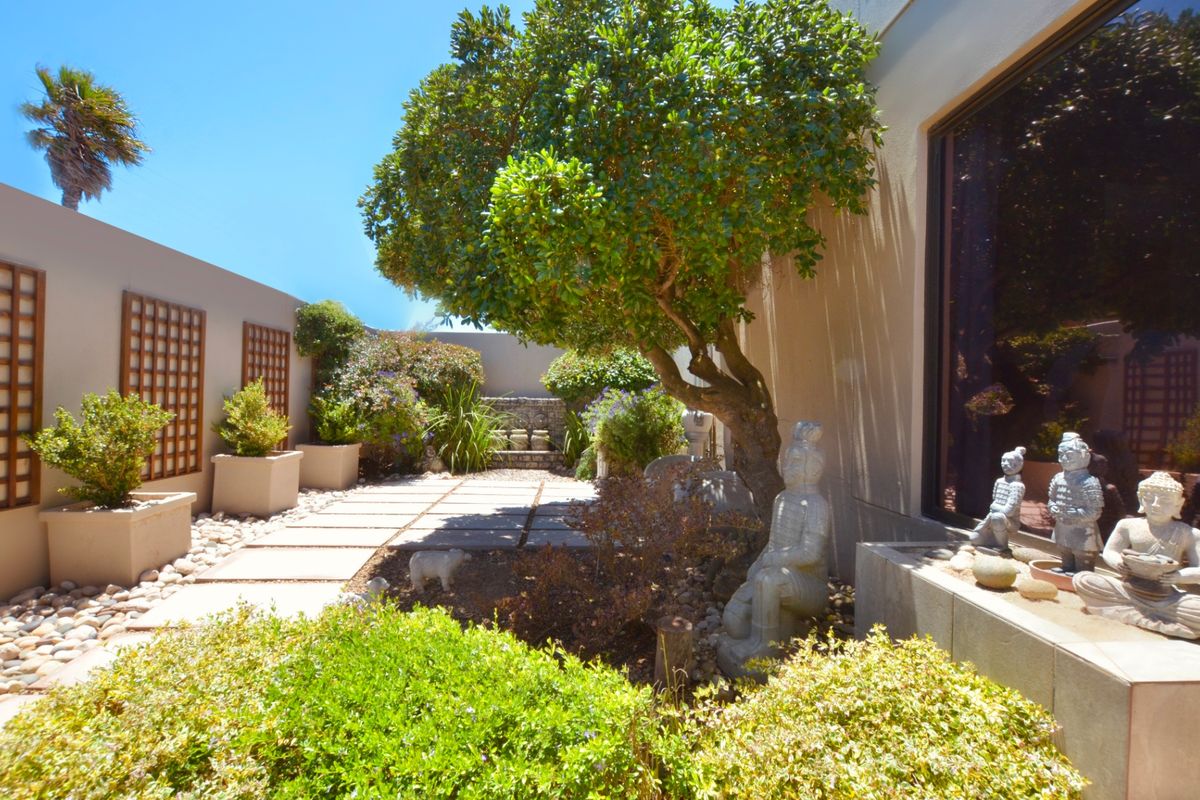 A tranquil, landscaped rear courtyard featuring paved pathways, established trees, and decorative wall trellises, creating a private outdoor retreat.