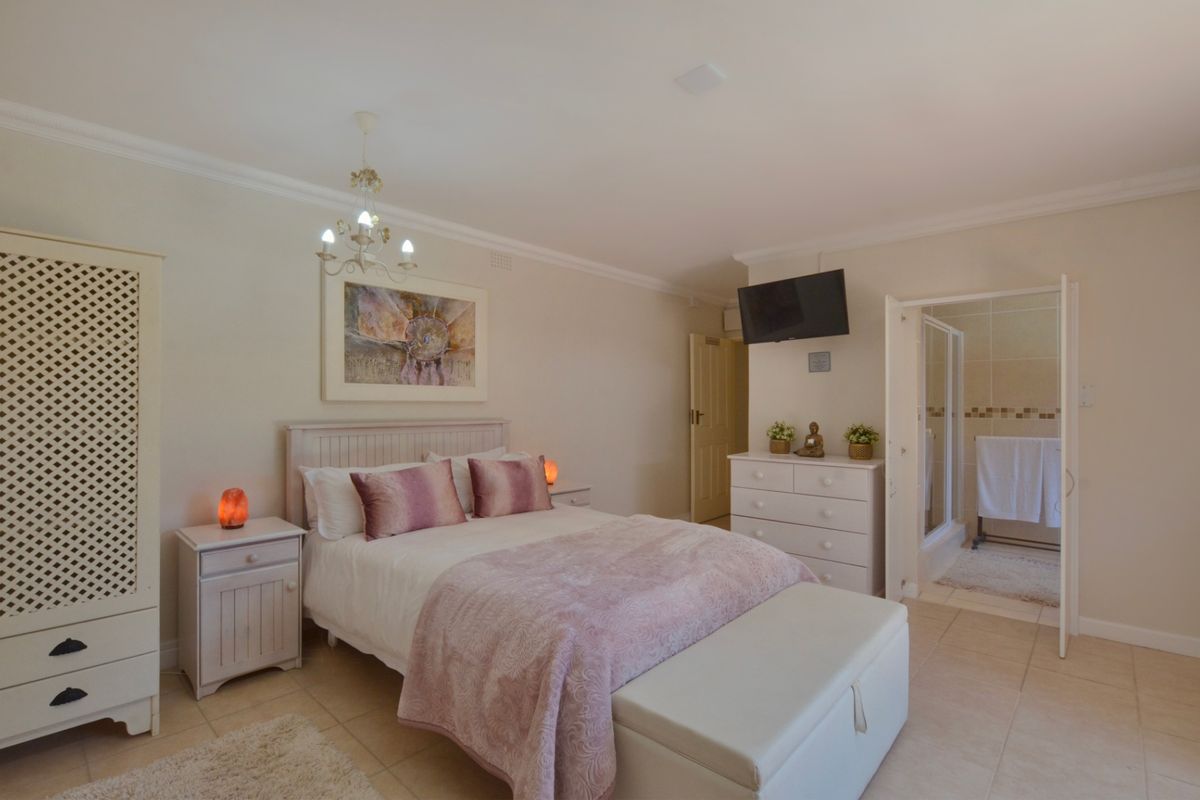 A well-maintained bedroom featuring tiled flooring, crown molding, and an en-suite bathroom with a shower.