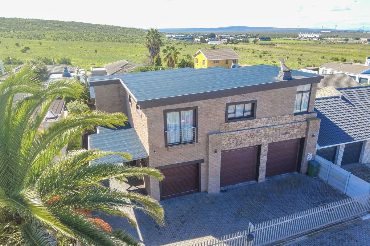 Aerial view of a double-story brick house featuring a triple garage, stone cladding accents, and a paved driveway in a suburban setting.