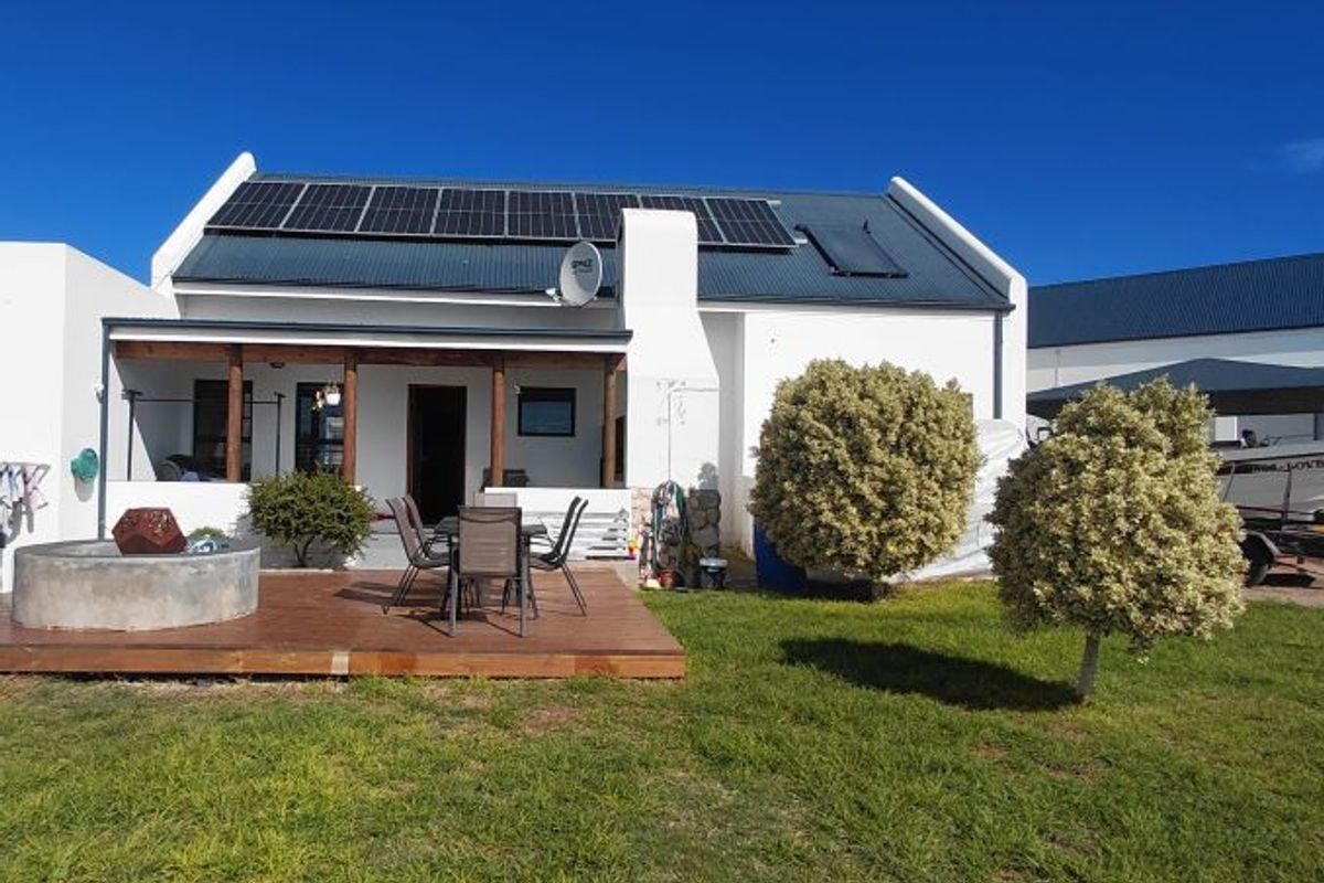 Rear view of the house featuring a covered patio, wooden deck, solar panels, and a well-maintained garden area.