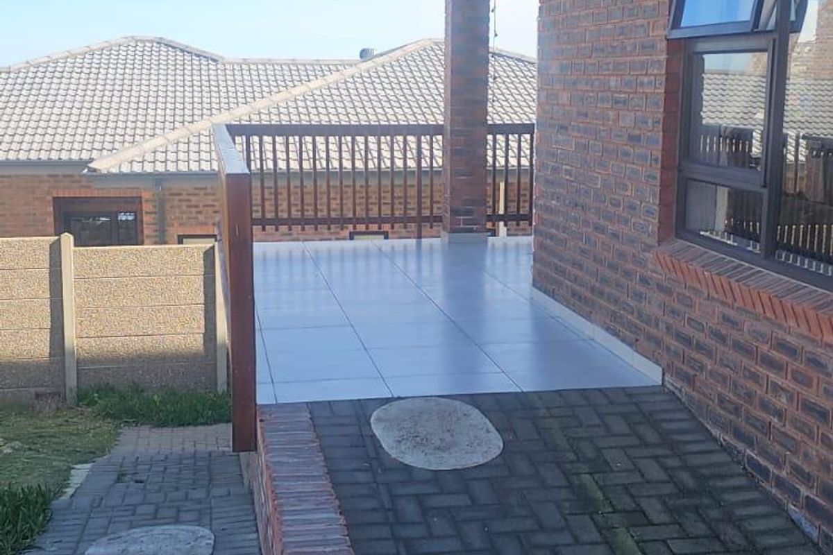 A paved exterior walkway leading to a tiled patio area with a brick facade and wooden balustrade.