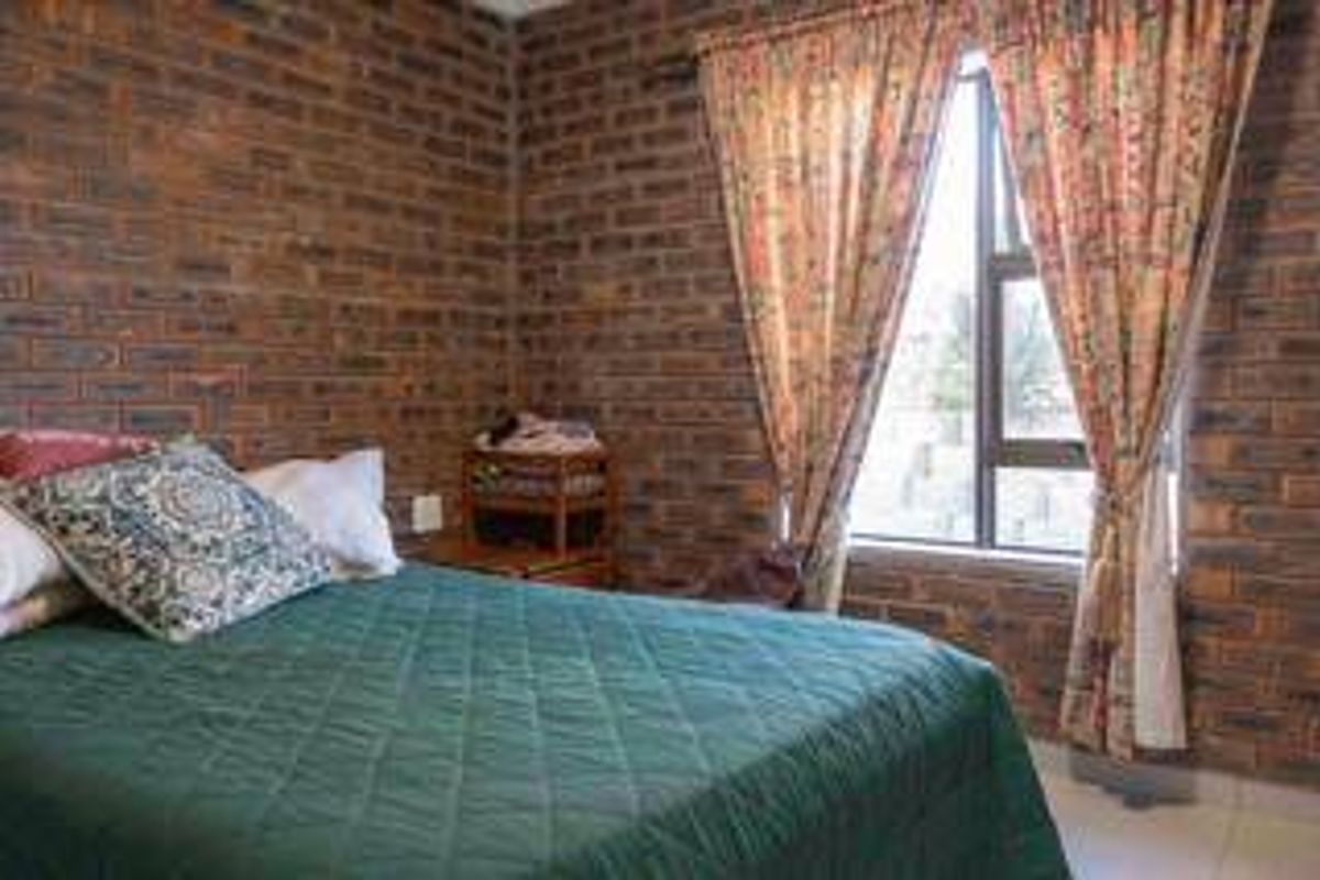 A bedroom featuring exposed face brick walls, tiled flooring, and a window with curtain treatments.