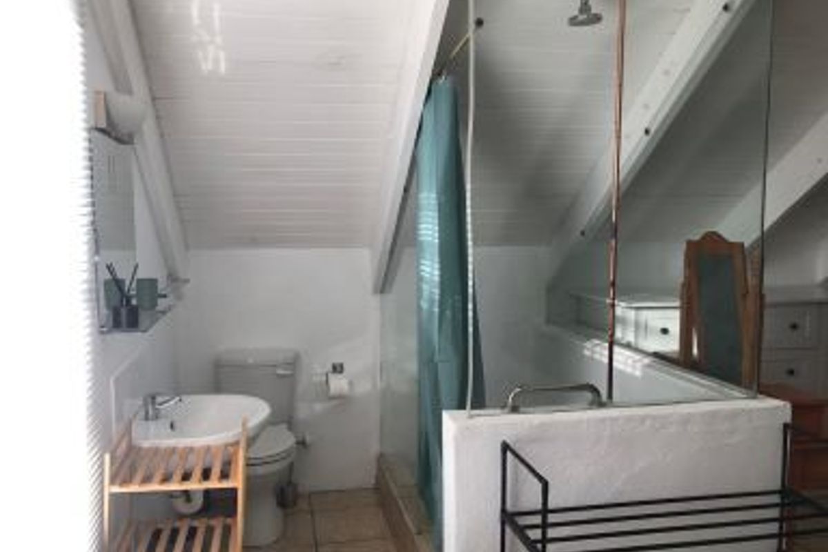 A compact attic-style bathroom featuring a shower, toilet, and pedestal basin with sloped timber ceilings and tiled flooring.
