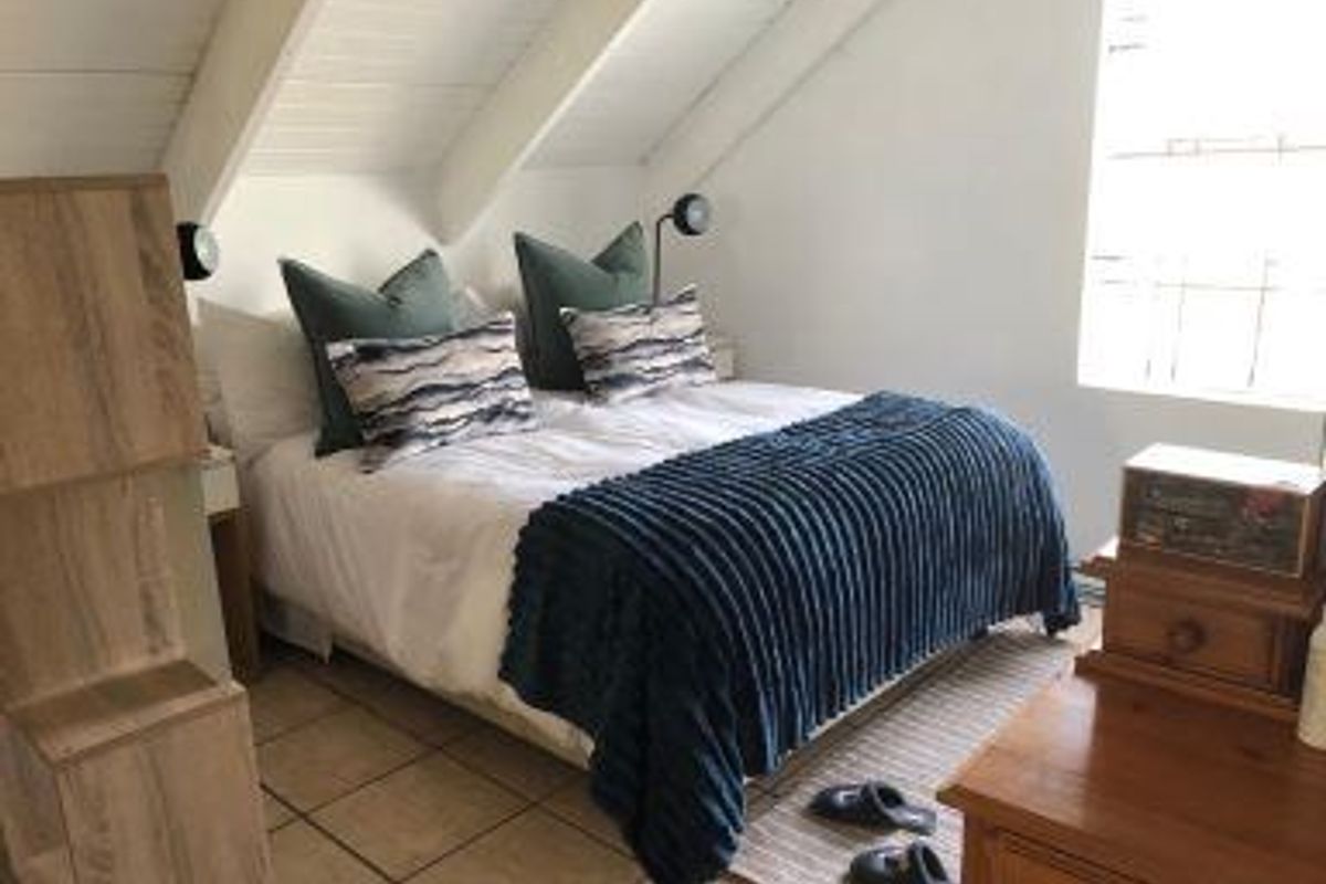 A cozy bedroom featuring a sloped ceiling with exposed beams, tiled flooring, and a window providing natural light.