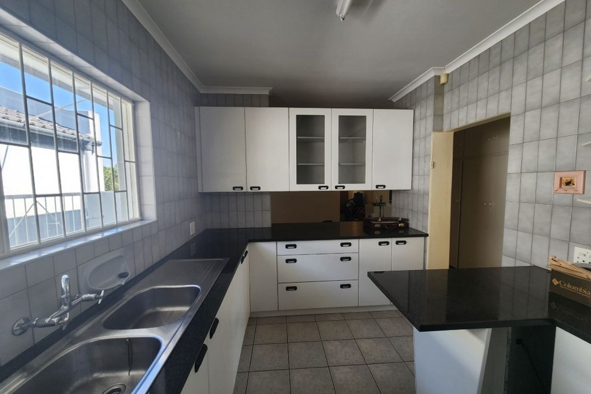 A functional kitchen featuring white cabinetry, dark granite countertops, a double stainless steel sink, and tiled walls and flooring.