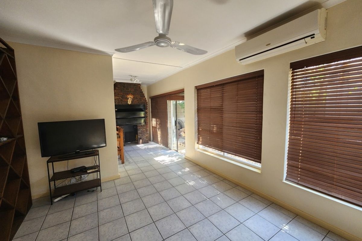 Living area featuring tiled flooring, a ceiling fan, wall-mounted air conditioning unit, and a brick fireplace, with access to an outdoor patio area.