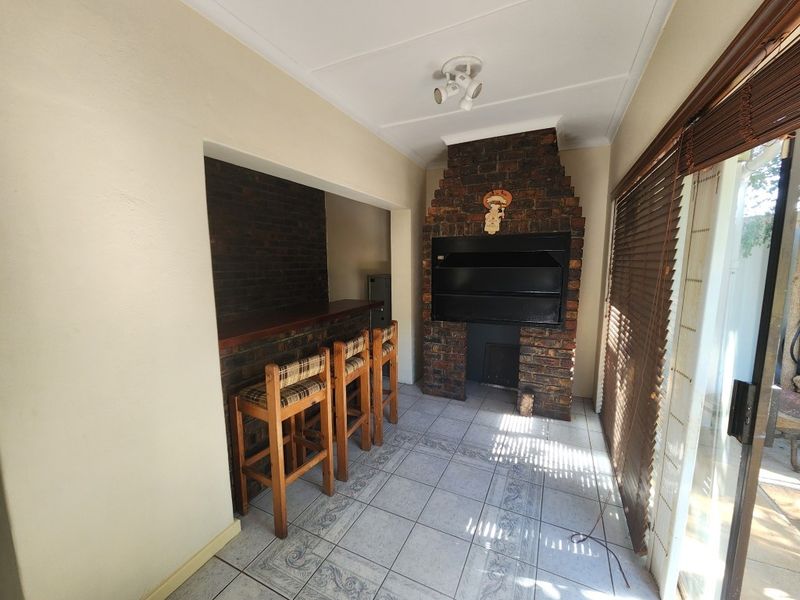 An indoor entertainment area featuring a built-in brick braai, a brick-faced bar counter, and tiled flooring with sliding door access to the exterior.