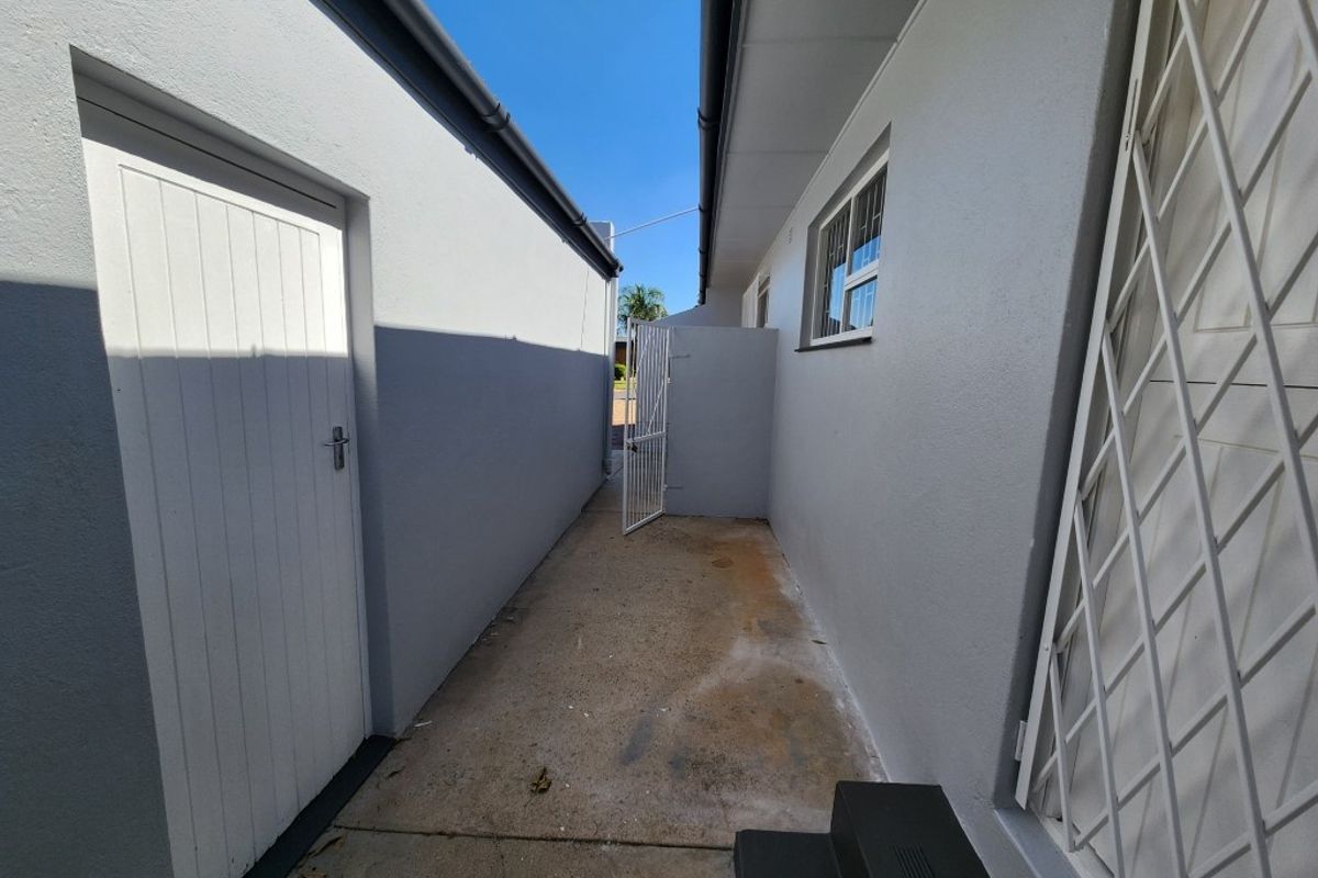 A narrow side passage or utility walkway featuring concrete flooring, exterior wall access, and a security gate.