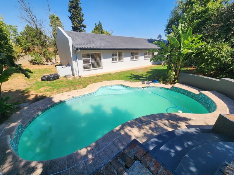 A rear view of the property featuring a swimming pool with tiled coping, set within a garden area adjacent to the house exterior.