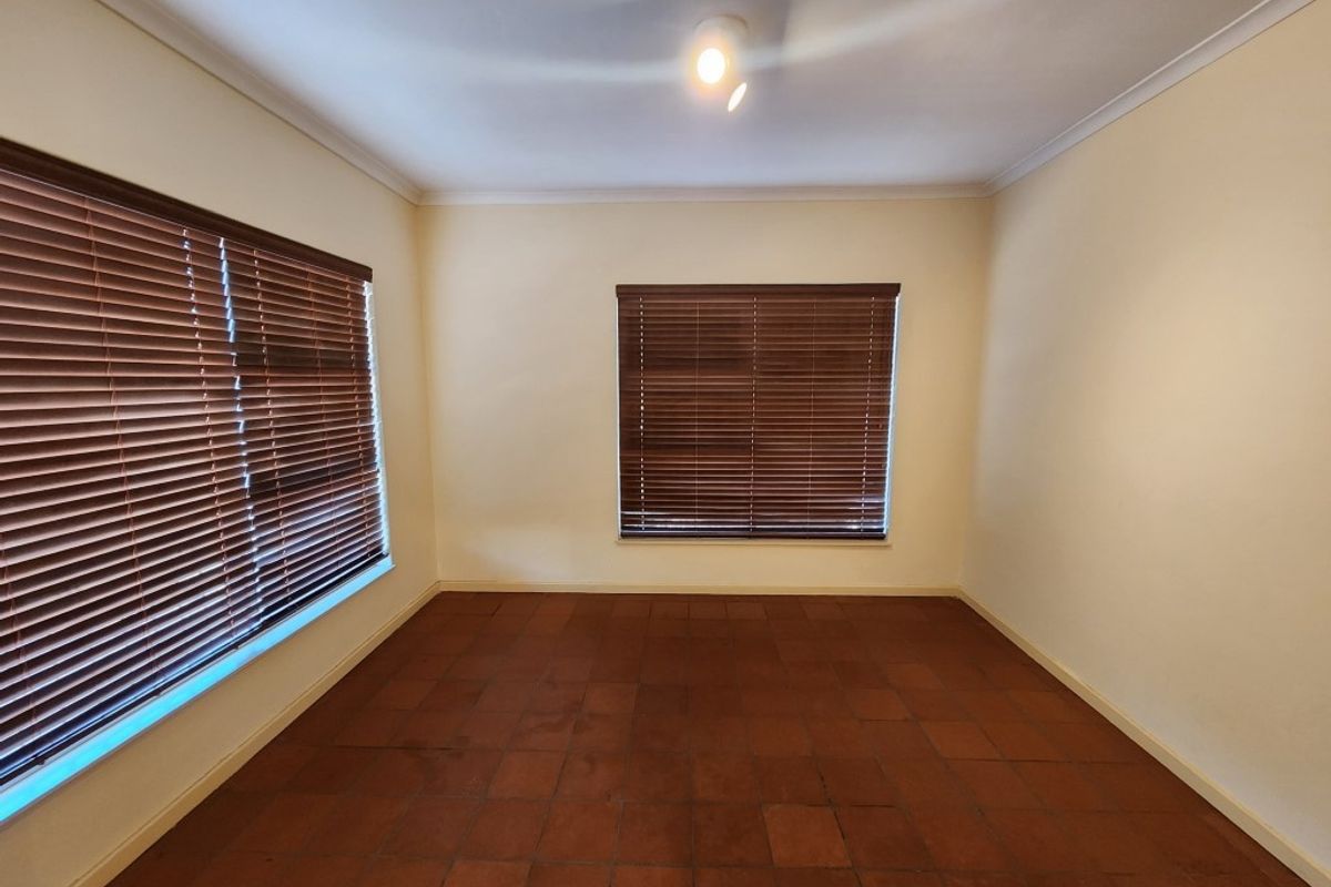 A bright, empty bedroom featuring terracotta floor tiles and fitted wooden venetian blinds.
