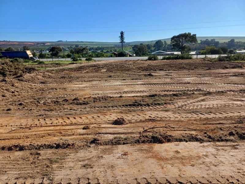 A wide-angle view of a cleared, undeveloped industrial plot of land with visible earthworks and surrounding landscape.