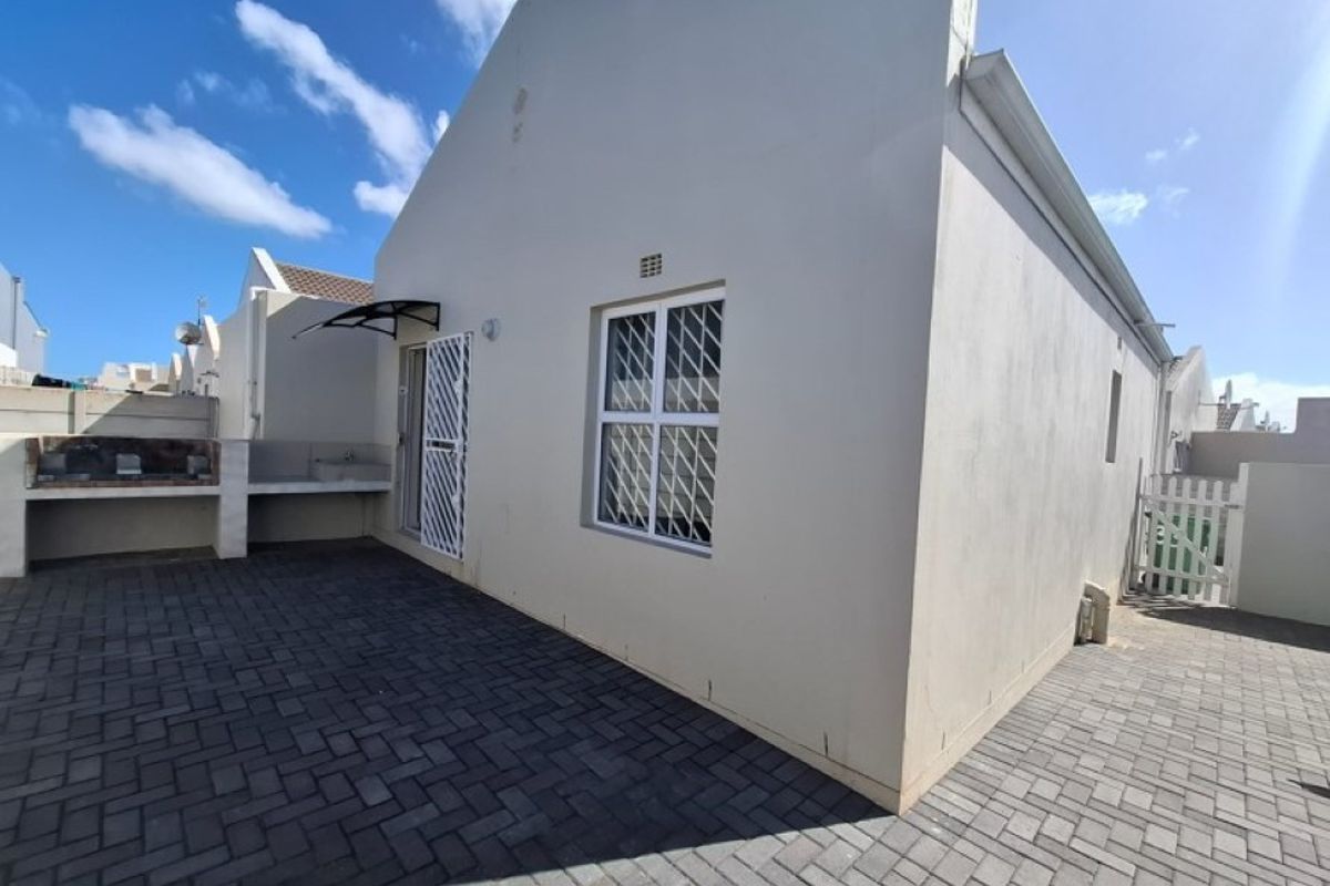 Rear exterior view of the property featuring a paved patio area, built-in braai, and security gates on windows and doors.