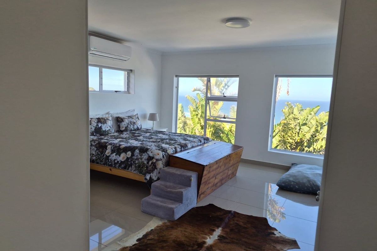 Spacious bedroom featuring large windows with ocean views, tiled flooring, and a wall-mounted air conditioning unit.