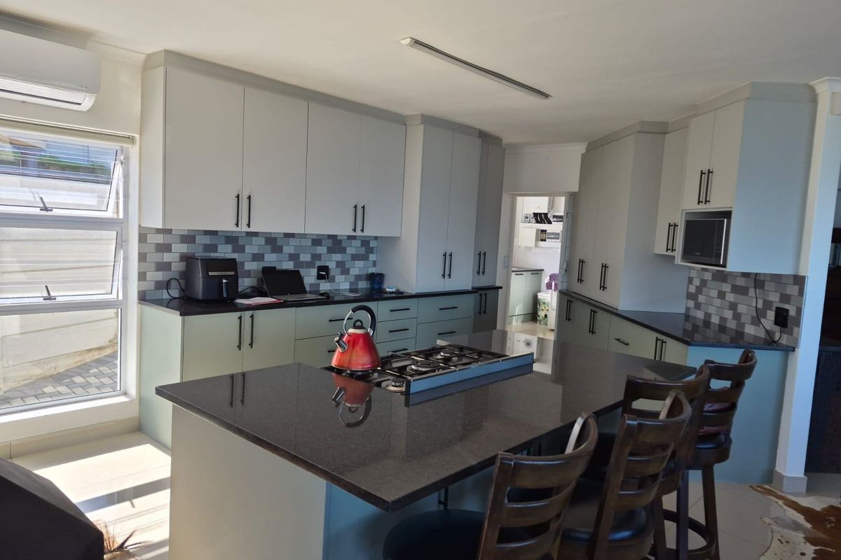 Modern kitchen featuring a central island with a built-in gas hob, stone countertops, ample cabinetry, and a tiled backsplash.