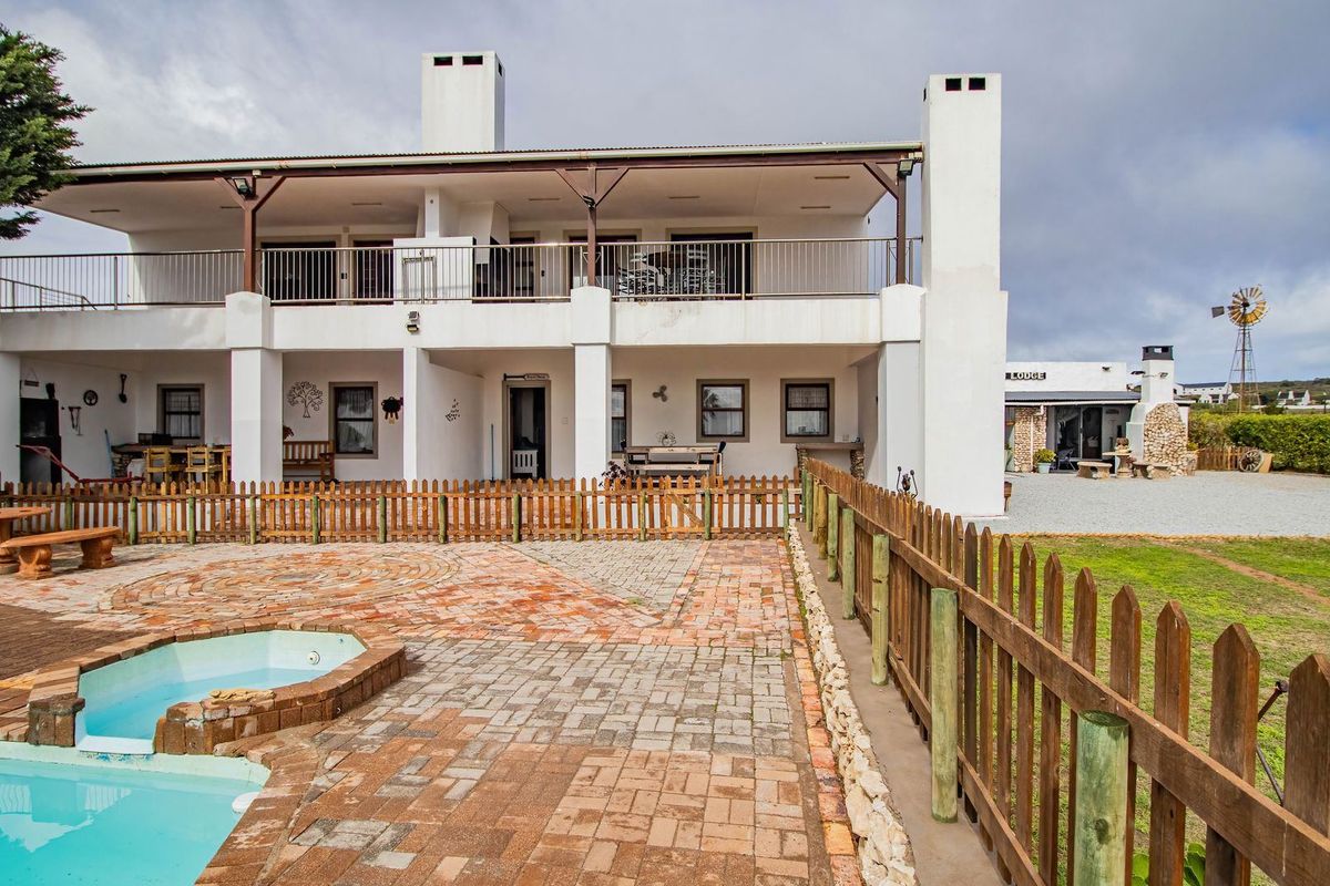 Rear view of a two-story house featuring a covered patio, balcony, swimming pool, and landscaped garden area with a windmill.