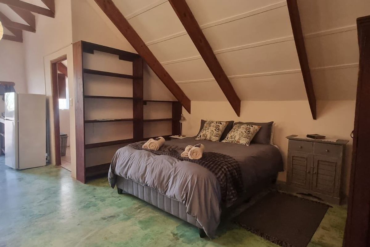 A bedroom featuring a vaulted ceiling with exposed timber rafters, built-in shelving, and polished concrete flooring, offering a rustic and open living space.