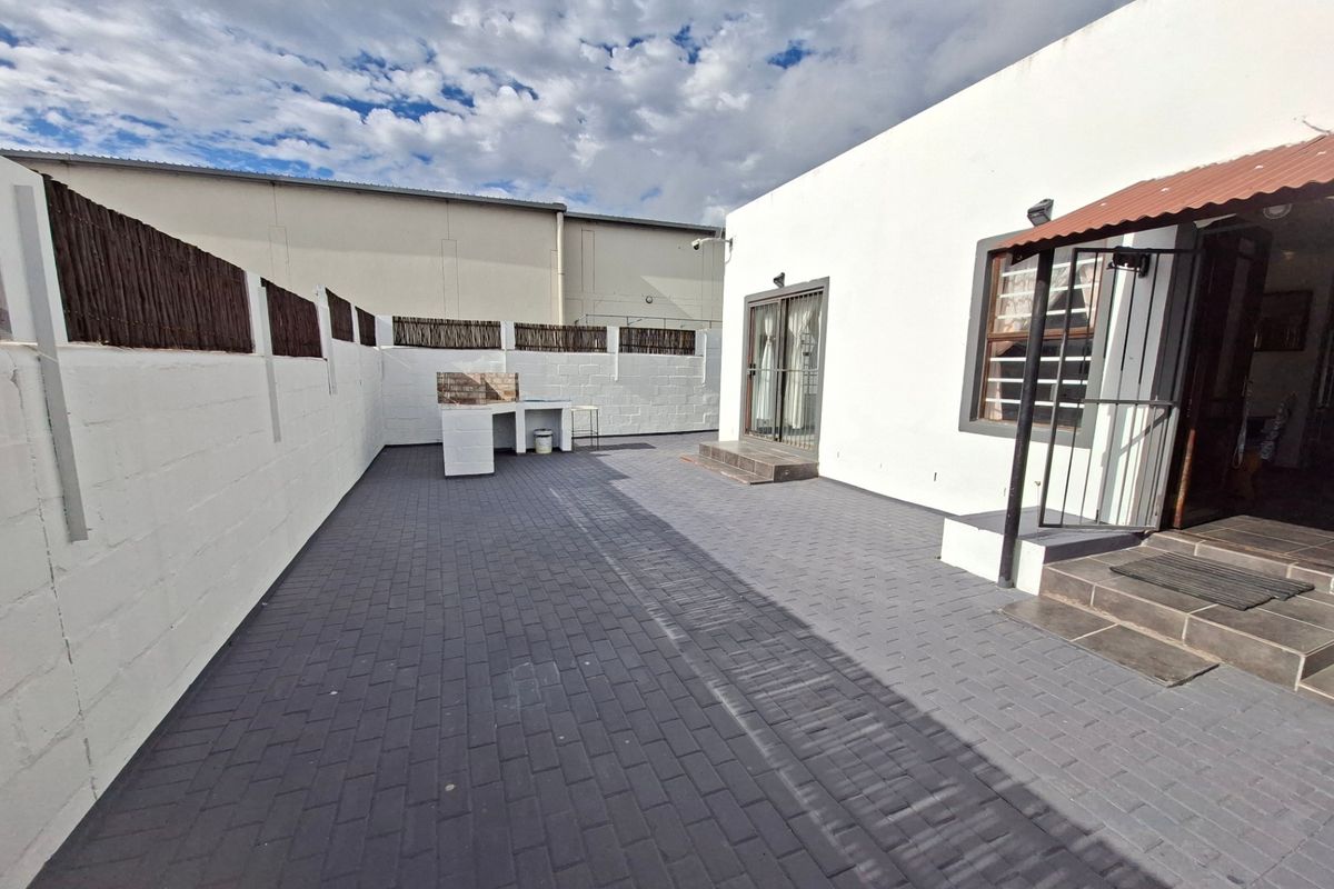 A paved rear courtyard featuring a built-in brick braai area, enclosed by white boundary walls with privacy screening.