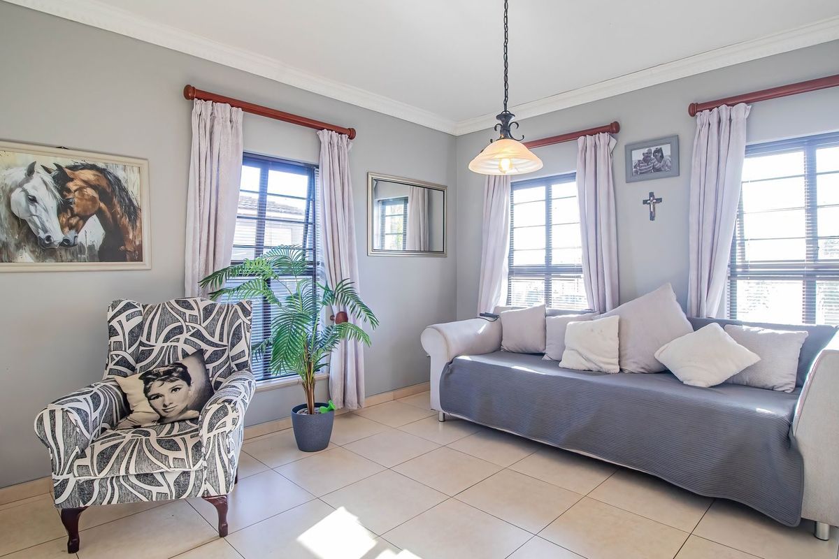 A bright and comfortable living room featuring neutral tiled flooring, crown molding, and large windows that provide ample natural light.
