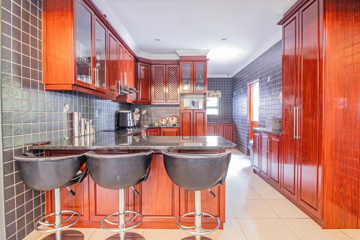 Spacious kitchen featuring dark wood cabinetry, granite countertops, a breakfast bar, and tiled walls throughout.