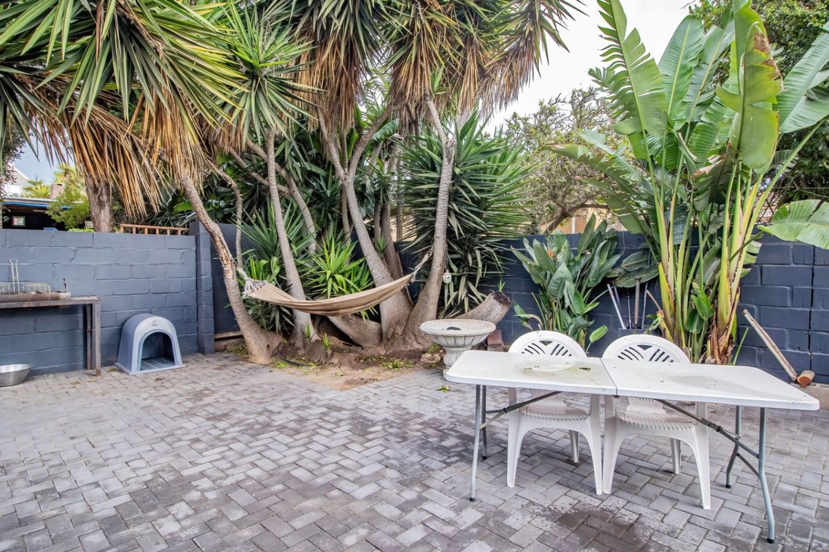 A private rear courtyard featuring paved flooring, a built-in brick braai area, and established garden landscaping with mature trees.