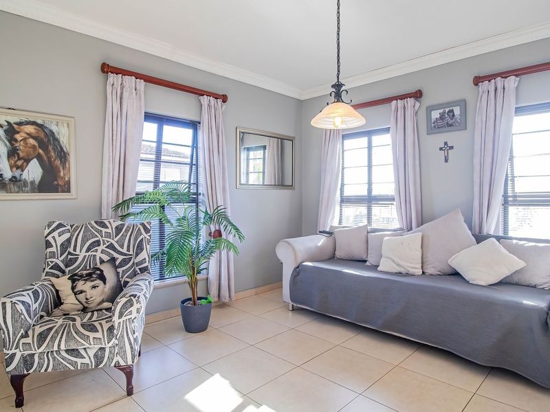 A bright and comfortable living room featuring neutral tiled flooring, crown molding, and large windows that provide ample natural light.