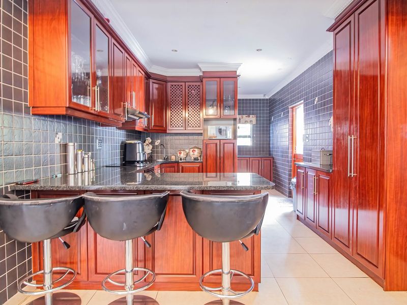 Spacious kitchen featuring dark wood cabinetry, granite countertops, a breakfast bar, and tiled walls throughout.
