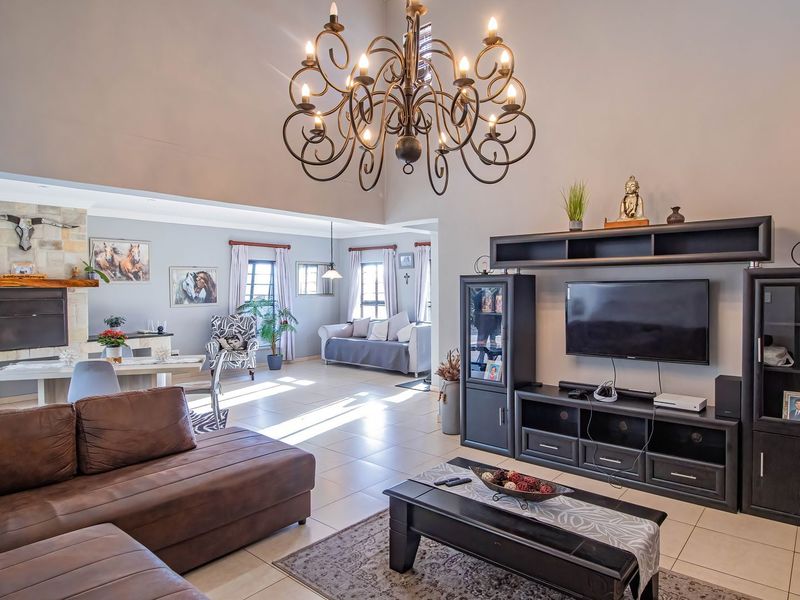 Spacious open-plan living area featuring high vaulted ceilings, a stone-clad fireplace, tiled flooring, and a large decorative chandelier.