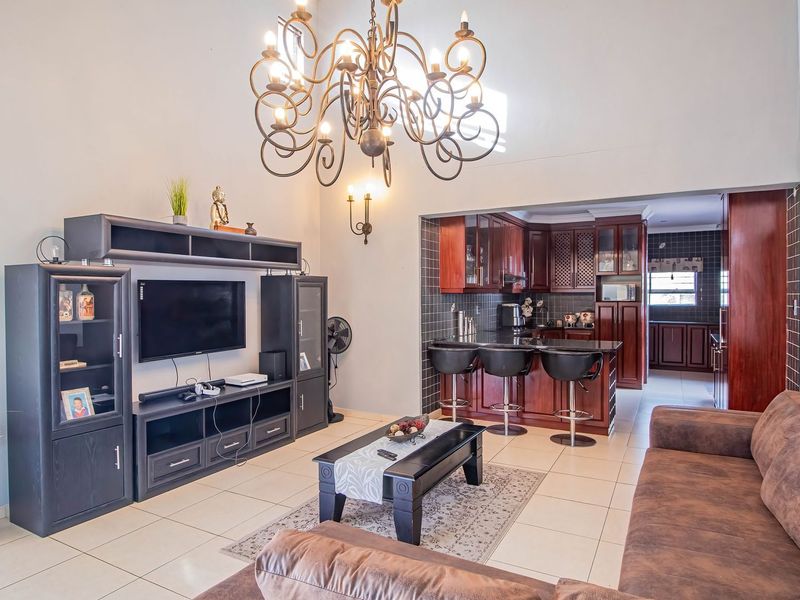 Open plan living area featuring a kitchen with dark wood cabinetry, tiled backsplash, and a breakfast bar, flowing into a spacious lounge with high ceilings.