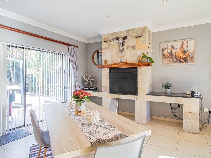 Dining area featuring a stone-clad built-in fireplace, tiled flooring, and large sliding glass doors providing direct access to the outdoor patio.