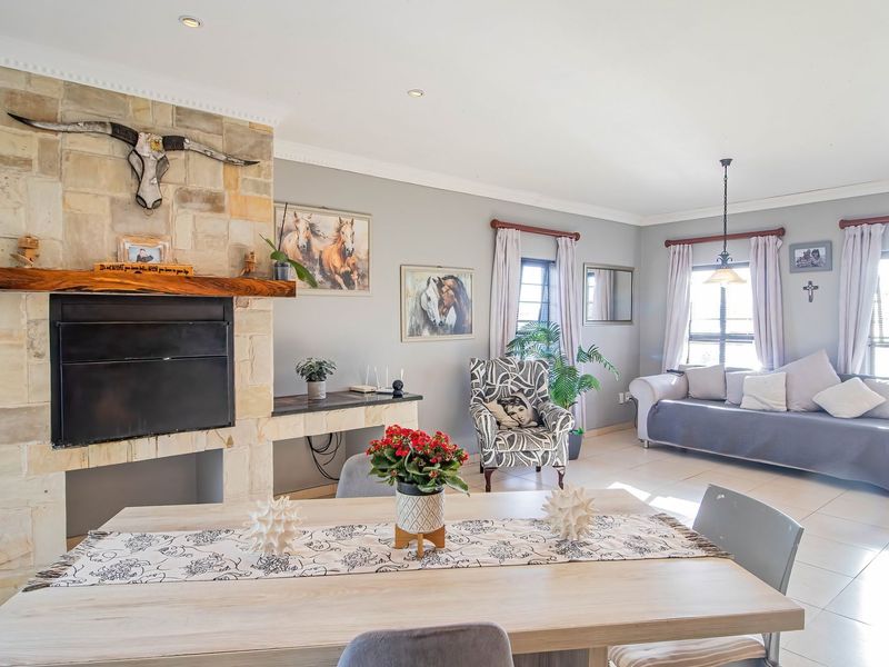 Spacious open-plan living and dining area featuring a prominent stone-clad fireplace, tiled flooring, and large windows providing ample natural light.