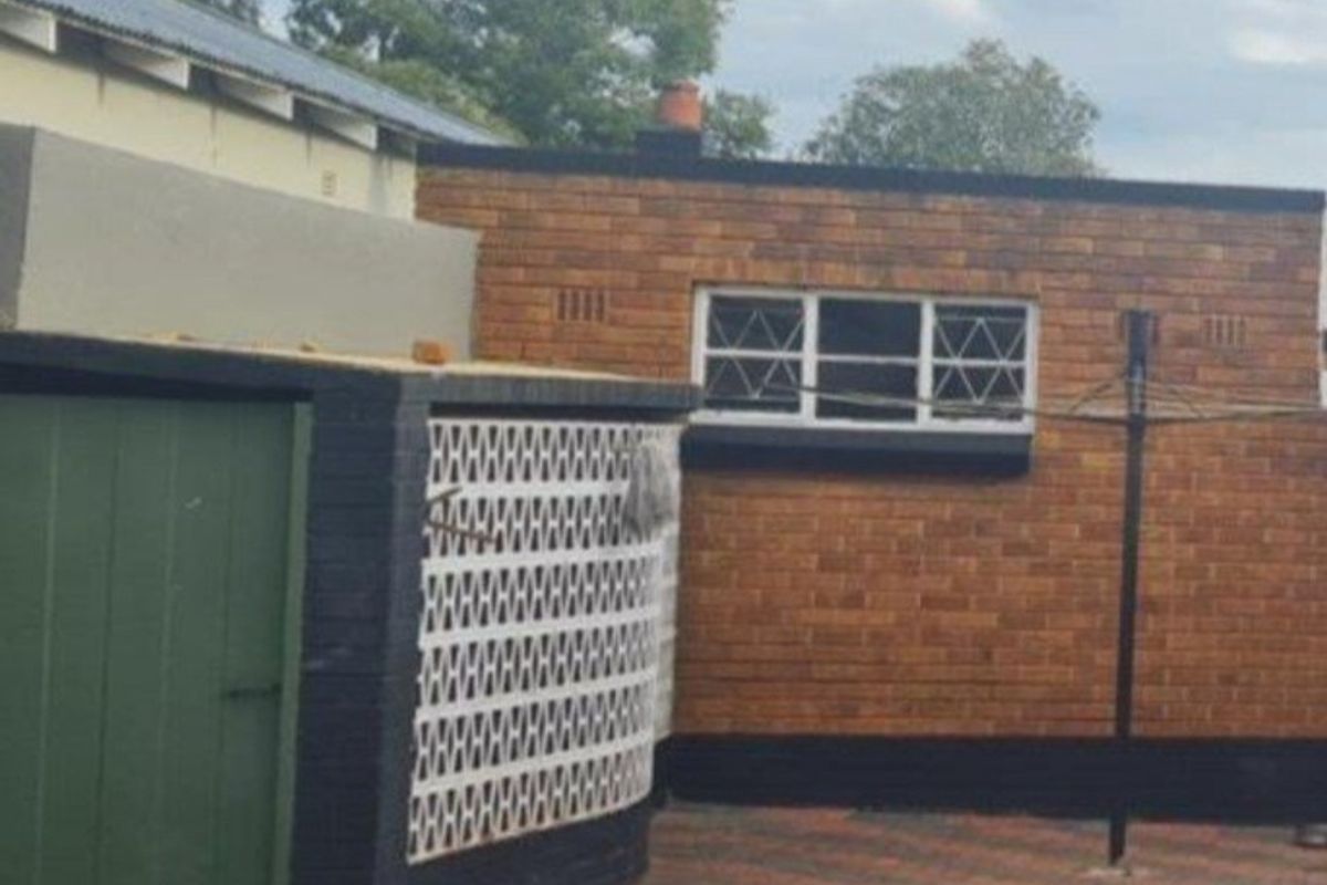 Rear exterior view of the property featuring face-brick walls, a paved courtyard area, and a secure side entrance door.