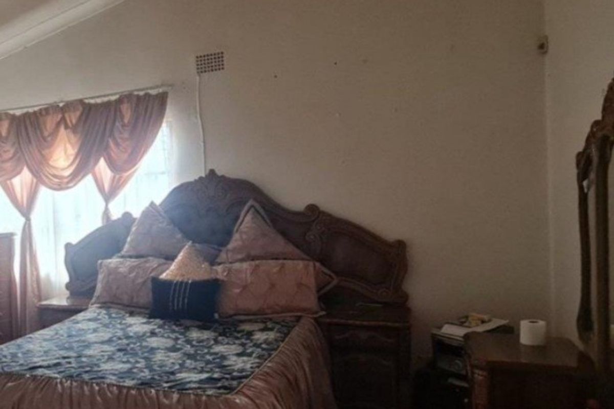 A bedroom featuring a vaulted ceiling and a window with draped curtains.