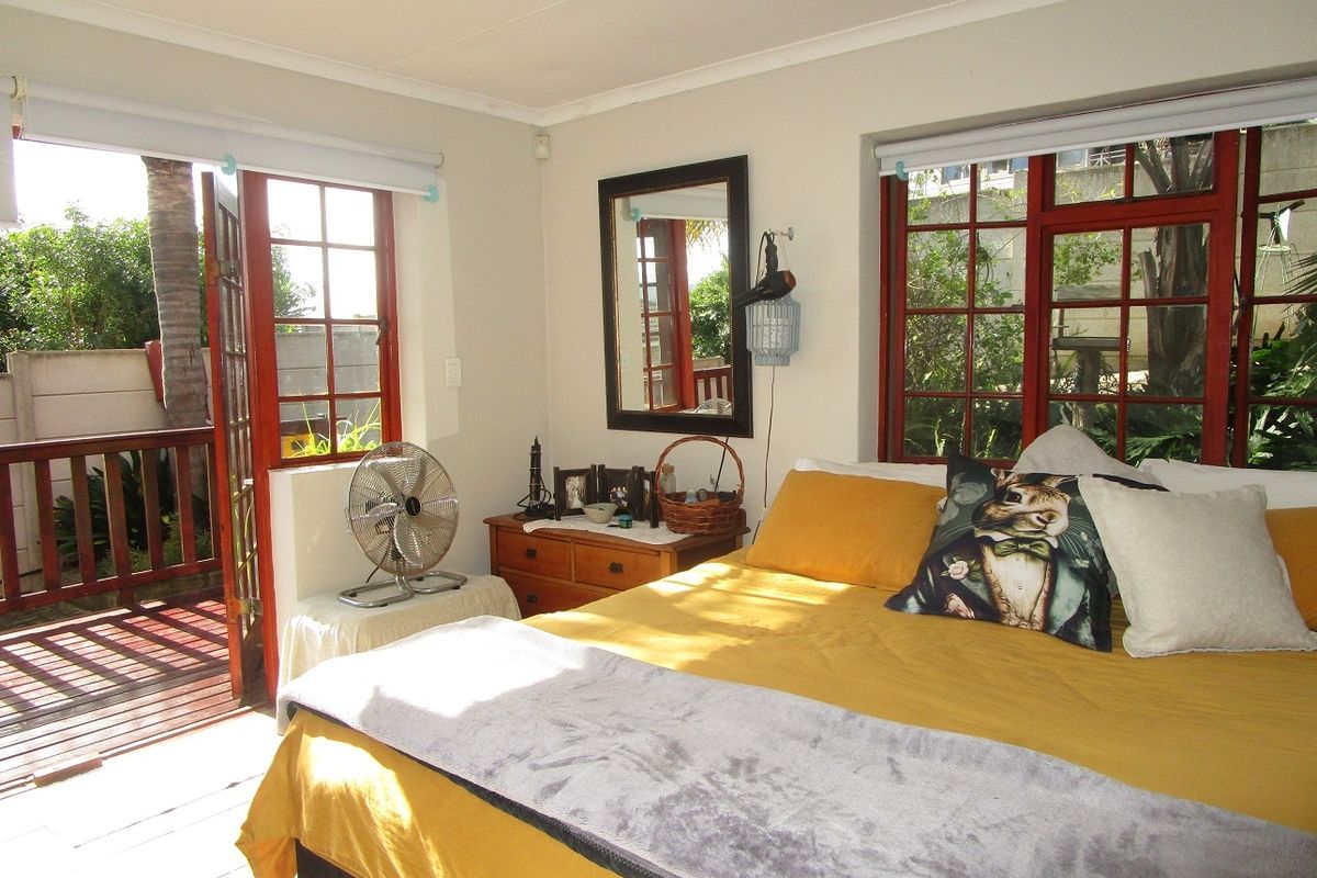 A bright bedroom featuring timber-framed windows and a private door leading directly to an outdoor deck area.