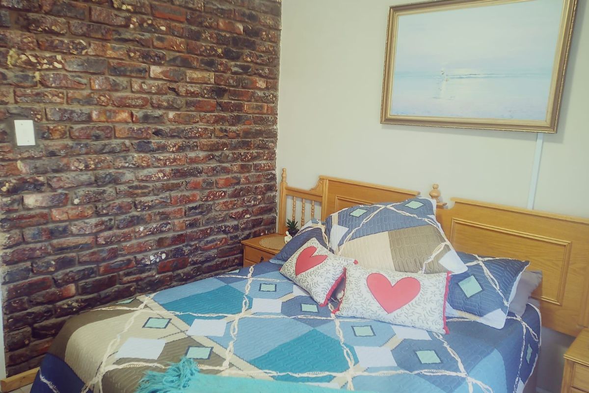 A bedroom featuring a rustic exposed brick feature wall and neutral painted walls.