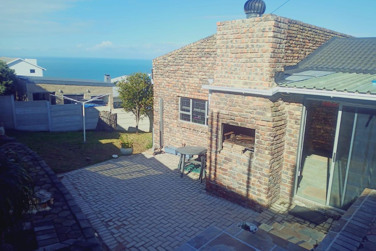 Rear patio area featuring a built-in brick braai, paved flooring, and direct access to the garden with distant ocean views.