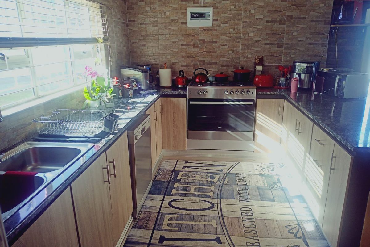 A functional kitchen featuring light wood cabinetry, dark granite countertops, a stainless steel oven with hob, and decorative stone-look wall tiling.