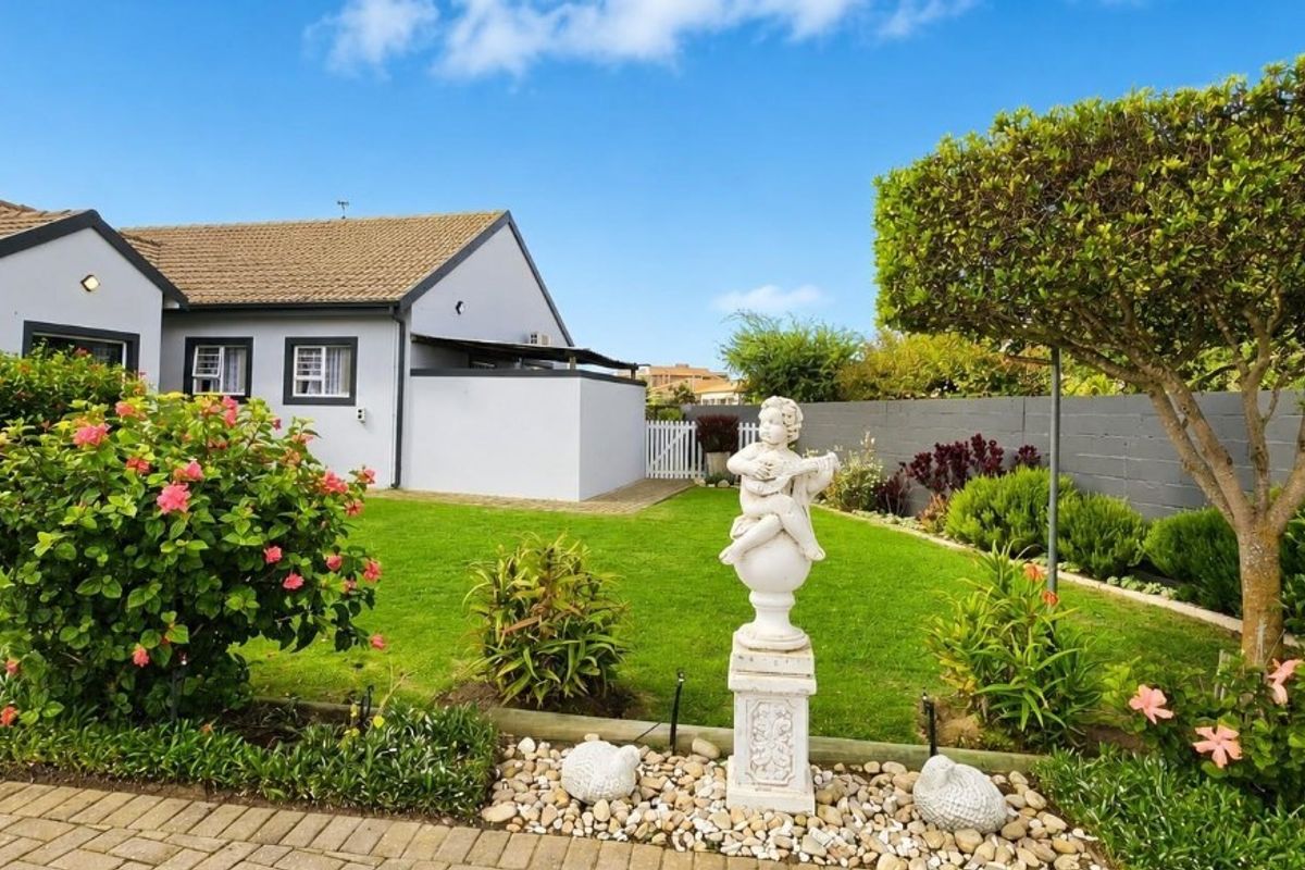 A well-maintained rear garden featuring a manicured lawn, paved areas, and established landscaping, adjacent to the rear elevation of the house.