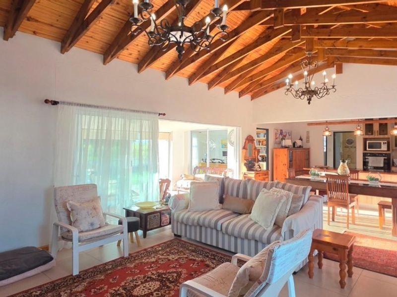 Spacious open-plan living and dining area featuring high exposed timber rafter ceilings, wrought iron chandeliers, and seamless flow to the kitchen and outdoor patio.