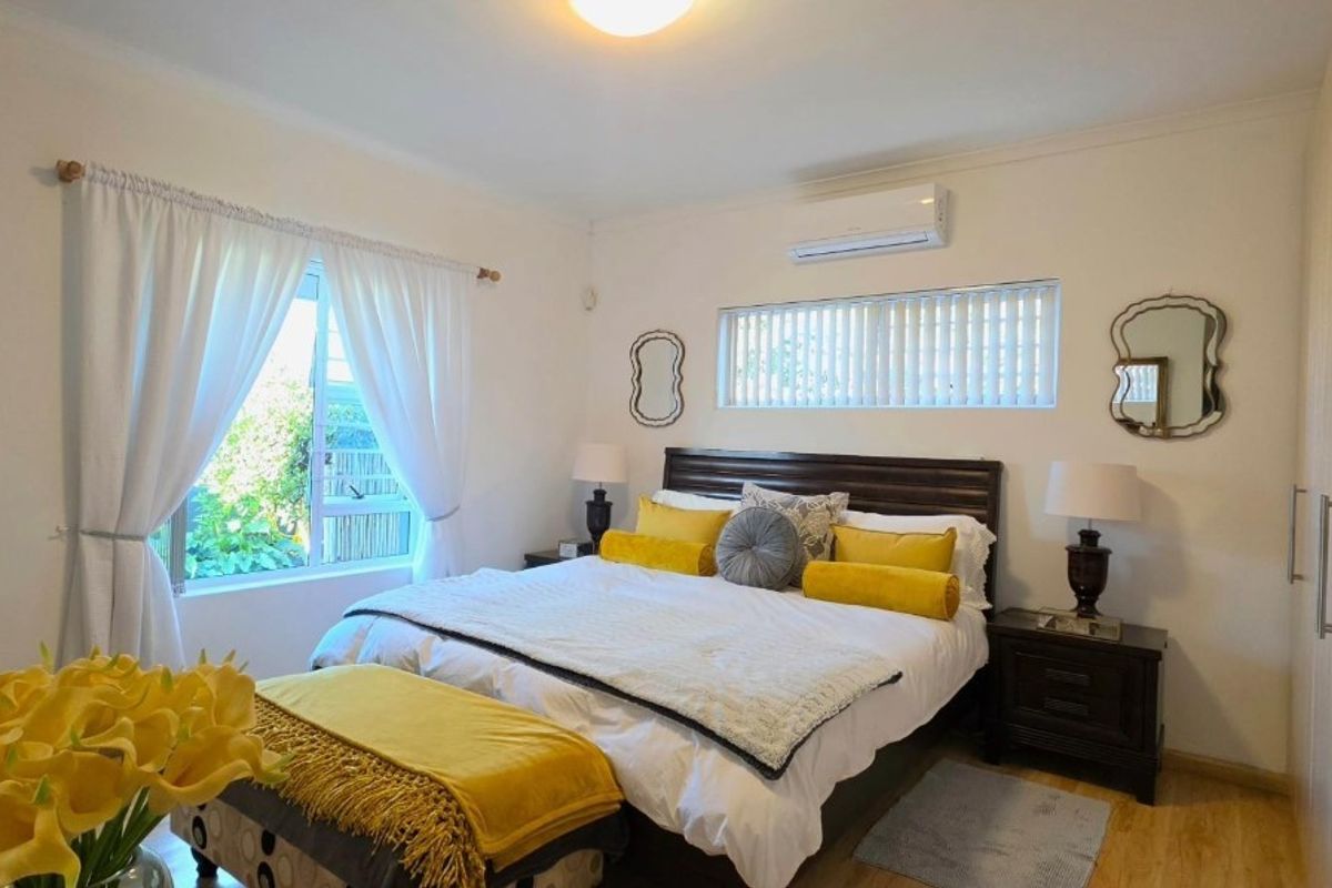 A well-maintained bedroom featuring laminate flooring, built-in cupboards, and a wall-mounted split-system air conditioner for climate control.