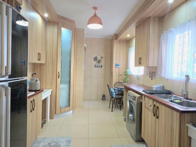 A functional kitchen featuring wood-look cabinetry, laminate countertops, tiled flooring, and integrated space for laundry appliances.