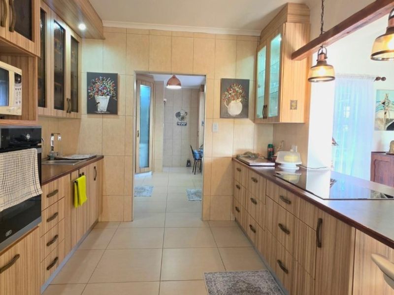 A well-maintained kitchen featuring wood-finish cabinetry, integrated appliances, tiled surfaces, and a breakfast bar overlooking the adjacent living area.