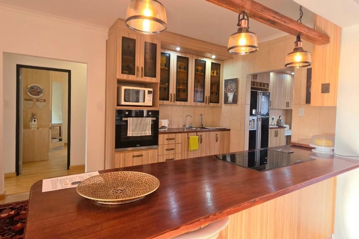 A well-maintained kitchen featuring wood-finish cabinetry, a built-in oven and microwave, a sleek hob, and a spacious wooden breakfast island with pendant lighting.